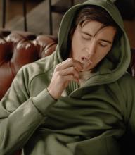 A man in a hoodie puts a stick of chewing gum in his mouth