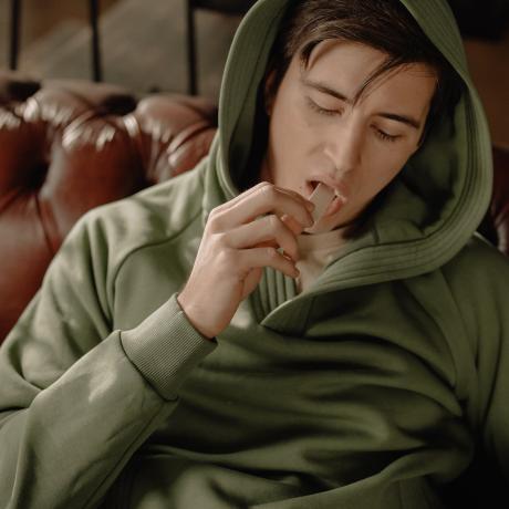 A man in a hoodie puts a stick of chewing gum in his mouth